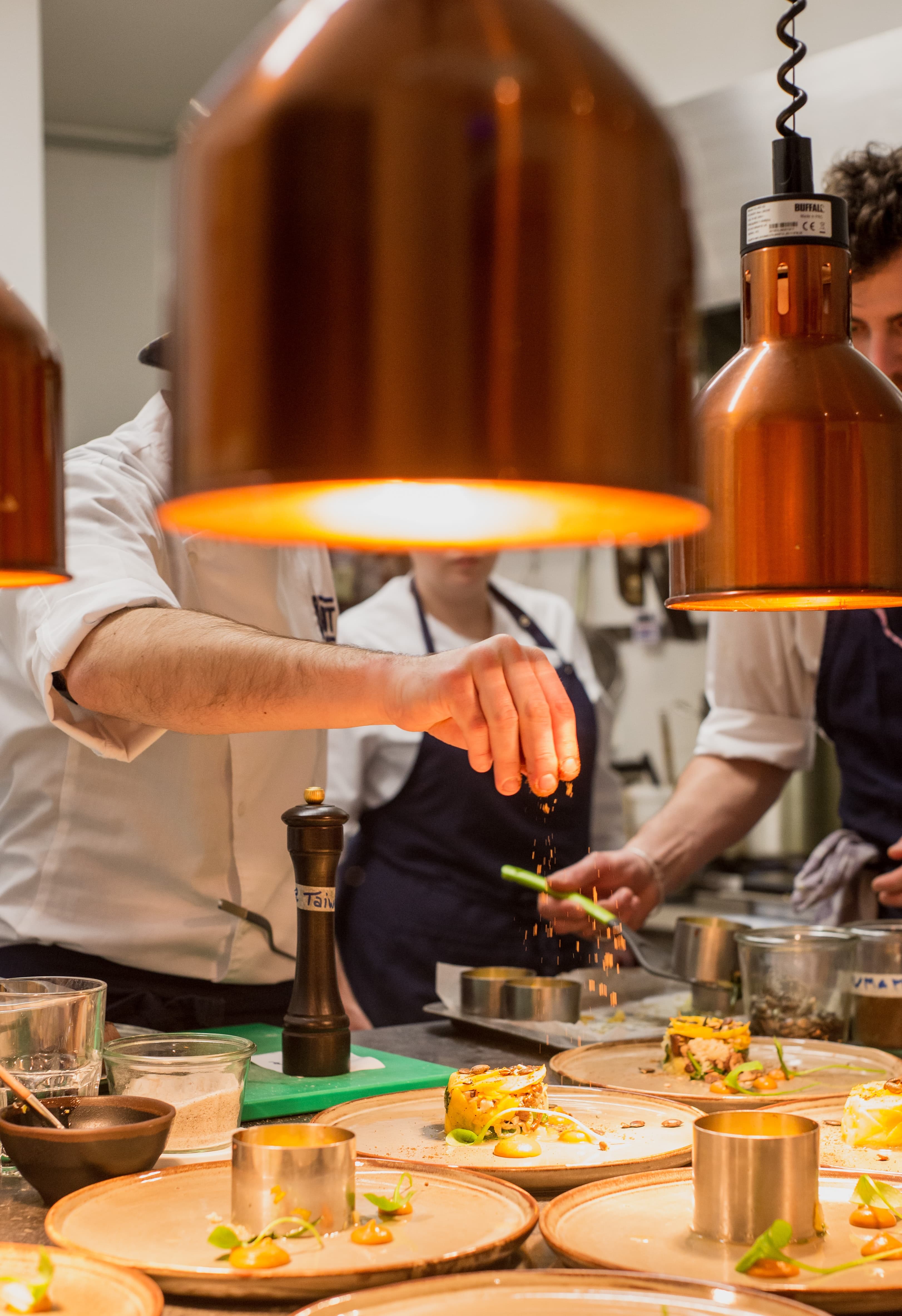 Chef die een gerecht opmaakt in een keuken met koperen lampen
